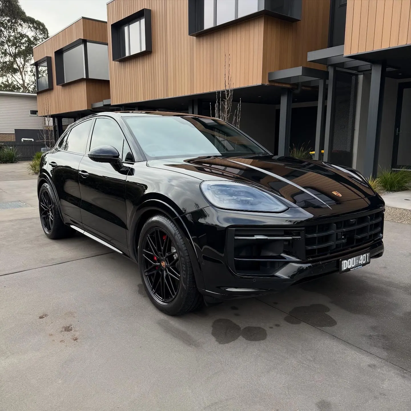 Black Porsche Cayenne Coupe GTS fully detailed, front three-quarter view outside luxury residence